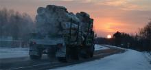 A loaded lumber truck drives a snowy highway at sunset